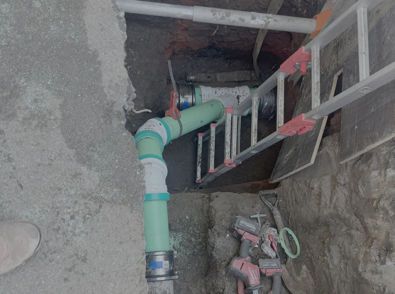 New PVC sewer lateral fittings installed in a shored excavation with an aluminum ladder for access