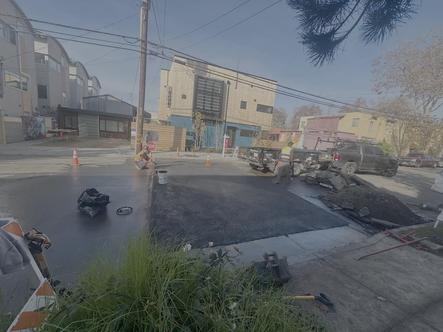 Fresh asphalt patch over a restored street cut after underground utility work, with the crew still on site