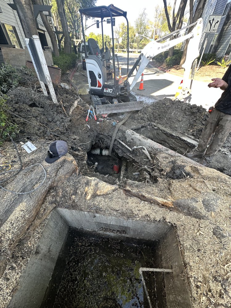 Excavation around a concrete utility box to reach a buried water line connection on a Bay Area property